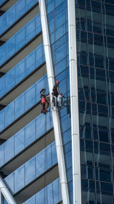 Vue de côté d'une jeune femme concentrée, portant des gants en latex, debout et en train de nettoyer un miroir dans une pièce lumineuse en journée